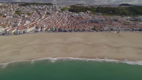 Aerial-trucking-shot-with-a-stunning-panorama-of-Nazare,-Portugal-with-its-famous-beach