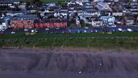 Aerial-drone-shot-dollying-backwards-out-from-a-residential-coastal-road-above-the-sandy-shore-of-Skerries-Beach,-Ireland