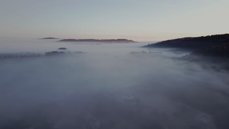 Aerial-view-of-mystical-and-tranquil-landscape-shrouded-in-thick-fog-during-dawn