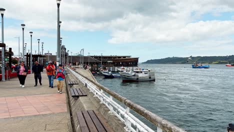 People-walking-Dalcahue-promenade,-traditional-craft-market-by-the-harbor,-Chiloé-Island