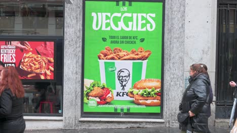 Fußgänger-Gehen-An-Einer-Straßenwerbung-Von-KFC-Vorbei,-Die-Ein-Neues-Vegetarisches-Gericht-Namens-Veggies-Vorstellt,-Das-In-Den-Fast-Food-Ketten-In-Spanien-Erhältlich-Ist