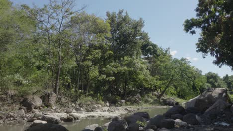 Dry-river-with-little-water-flow-with-many-rocks-and-leafy-trees,-affected-by-climate-change-in-Honduras