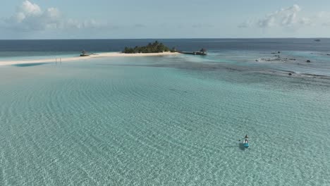 Remote-tropical-island-with-woman-paddleboarding-in-shallow-water,-aerial