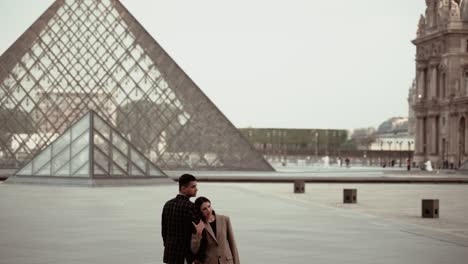 Elegante-Pareja-Abrazándose-Suavemente-En-Una-Pose-Artística-De-Ensueño-Disfrutando-Del-Momento-Sin-Turistas-En-El-Museo-Del-Louvre-En-París,-Francia,-Rodeado-De-Edificios-Barrocos-De-Residencia-Real---Ancho