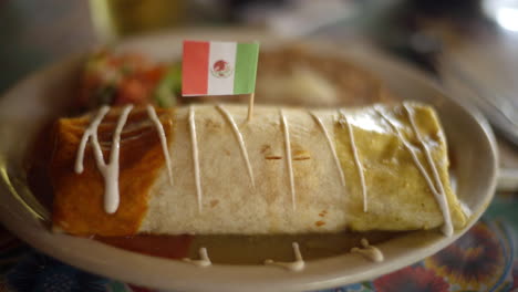 A-delightful-video-captures-an-authentic-burrito-adorned-with-savory-white-sauce-and-accompanied-by-a-Mexican-flag,-enhancing-the-essence-of-this-traditional-Mexican-cuisine