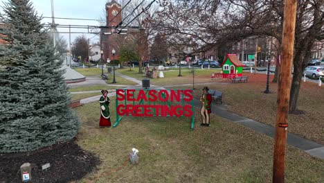 Weihnachtsgrüße-Zeichen-Im-Park-Neben-Weihnachtsbaum-Und-Kirche-Im-Hintergrund