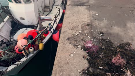 A-fishing-boat-moored-to-concrete-docks,-adorned-with-colorful-buoys,-embodying-the-maritime-essence-of-a-small-fishing-town