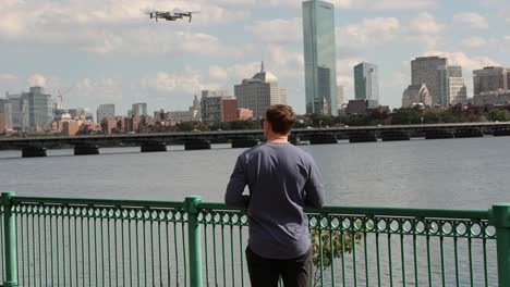 Creador-De-Contenido-Masculino-Lanzando-Drone,-Horizonte-De-Boston-En-Segundo-Plano
