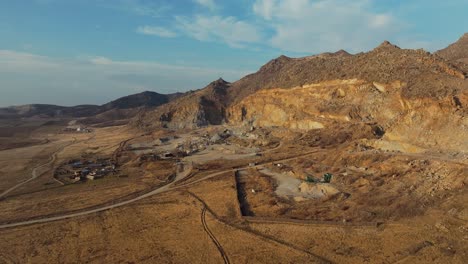 Stone-quarry-aerial-wide-shot-at-the-base-of-old-mountains-,-sunny-day-blue-sky