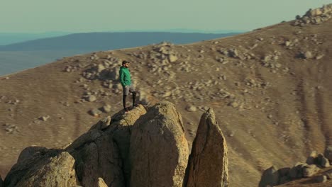 Lone-hiker-stands-atop-a-mountain-peak-slow-parallax-drone-shot