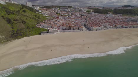 Aerial-trucking-shot-with-a-stunning-panorama-of-Nazare,-Portugal-with-its-sandy,-empty-beach