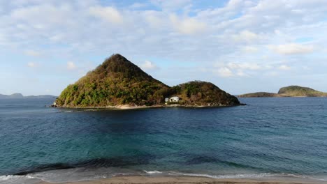 Abgeschiedene-Tropische-Insel-Mit-üppigem-Grün-Und-Einem-Einzigen-Haus,-Blauem-Ozeanwasser,-Ruhiger-Atmosphäre,-Tageslicht