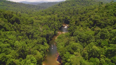 A-lush-jungle-in-oxapampa,-peru-with-a-river-snaking-through-and-a-small-waterfall,-daylight,-aerial-view