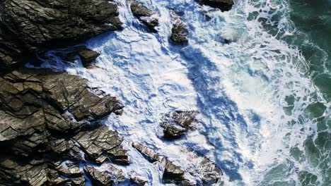 Rotating-Top-Down-View-of-Ocean-Waves-and-White-Water-Splashing-Over-Cornish-Slate-Rocks