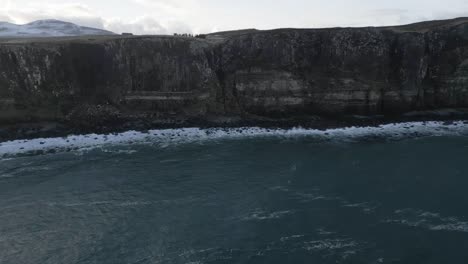 Blick-Von-Der-Klippe-Auf-Kilt-Rock-In-Schottland-Mit-Schneebedeckten-Bergen-In-Der-Ferne-Und-Wellen,-Die-Ans-Ufer-Brechen