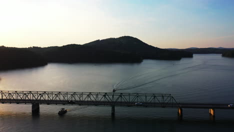 Erstaunliche-Luftaufnahmen-Von-Booten,-Die-Bei-Sonnenuntergang-Unter-Einer-Straßenbrücke-Hindurchfahren