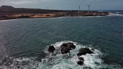 Sea-foam-surrounding-stones-and-windmills-on-coast-of-Corralejos-beach,-Fuerteventura