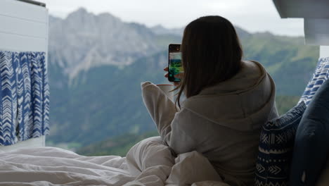 Junge-Frau-Hält-Eine-Tasse-Kaffee-In-Der-Hand-Und-Fotografiert-Mit-Dem-Smartphone-Die-Dolomiten-Vom-Bett-Im-Reisebus-Aus