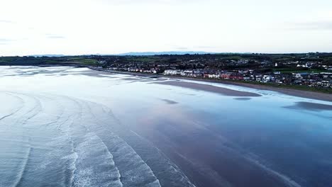 Eine-Drohnenaufnahme-Der-Malerischen-Irischen-Seeküste-Mit-Ruhigen-Wellen,-Die-Bei-Sonnenaufgang-Am-Strand-Von-Skerries-In-Dublin,-Irland-Ans-Ufer-Rollen