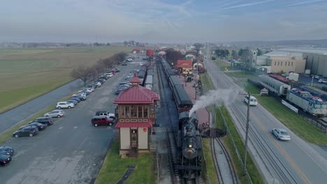 An-Aerial-View-of-a-Train-Station,-with-a-Steam-Passenger-Train,-Disconnecting-from-the-Coaches,-Blowing-Smoke,-on-a-Partially-Sunny-Day