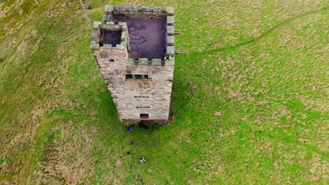 Old-derelict-castle,-monument,-disused-stone-tower,-with-people-walking-around-and-flying-a-drone