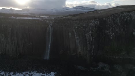 Majestuosa-Cascada-De-Roca-Escocesa-En-Skye,-Escocia,-Con-Montañas-Cubiertas-De-Nieve-Al-Fondo-Al-Atardecer