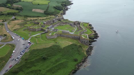 Charles-fort-in-kinsale,-ireland-with-lush-greenery-and-a-boat-on-the-water,-aerial-view
