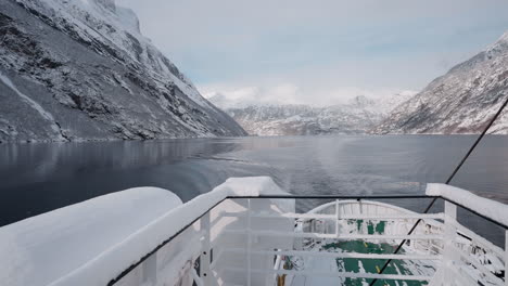 POV-video-of-a-ferry-ride-through-Geirangerfjord-in-winter,-featuring-stunning-views-of-snow-covered-mountains,-a-bright-sky,-and-reflections-in-the-fjord