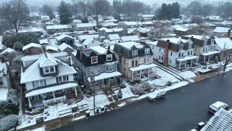 Snowflakes-over-a-residential-street-with-row-houses,-bare-trees,-and-parked-cars