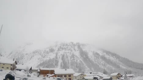 Pan-shot-of-snowy-mountain-side-with-village-at-bottom-on-a-cloudy-cold-day