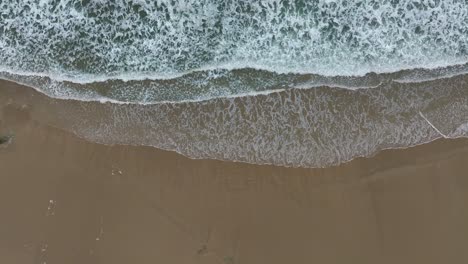 Sea-Foamy-Water-Waves-Crashing-On-Sandy-Beach---Aerial-Top-Down