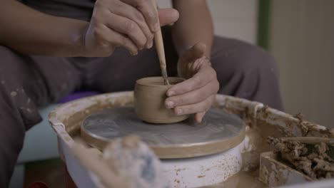 Skilful-craftsman-concentrates-cutting-clay-pot-on-turntable-with-ribbon-tool-SLOW-MOTION