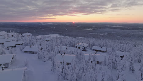 Aerial-view-backwards-over-snowy-mountain-cabins,-winter-morning-in-Lapland