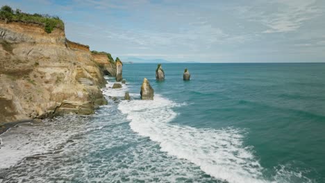 Waves-breaking-on-coastal-landscape-with-large-sea-stack-columns,-aerial