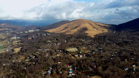 A-small-town-nestled-among-autumn-hills-under-a-cloudy-sky,-dramatic-lighting,-aerial-view