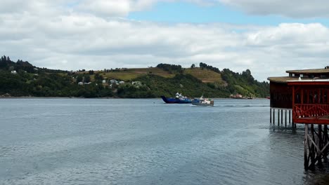 Escena-Tranquila-Del-Paseo-Marítimo-De-Dalcahue,-Barco-Navegando-Por-La-Costa,-Toma-Panorámica