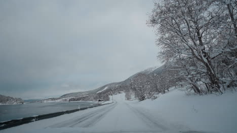 POV-drive-through-Norway's-western-fjord-on-a-snowy-winter-day,-featuring-beautiful-snowy-mountains-and-roads