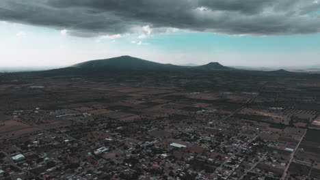 Drone-video-over-Nopaltepec,-Mexico,-featuring-city-views,-distant-mountains,-and-dark-clouds-in-a-rural-setting