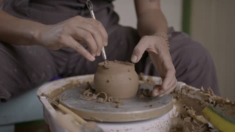 Potter-carefully-uses-ribbon-tool-for-refine-cutting-of-rotating-clay-pot-SLOW-MOTION