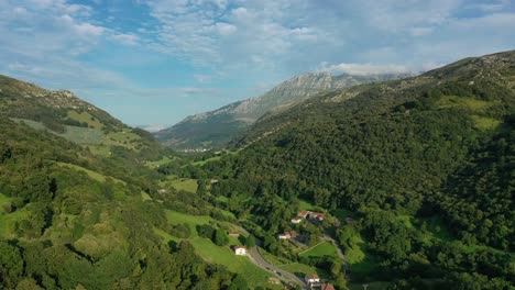 Vuelo-De-Drone-En-Un-Pequeño-Valle-Visualizando-Un-Pueblo-Con-Su-Camino-Y-Praderas-De-Cultivo-Y-Ganadería-Con-Sus-Bosques-De-Robles-Y-Hayas-Con-Un-Fondo-De-Montañas-De-Piedra-Caliza-En-Cantabria-españa