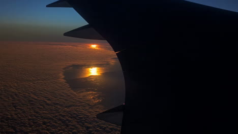 Stunning-footage-of-white-clouds-below-from-airplane-window-with-sun-setting-in-the-background-along-blue-sky