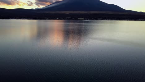 Mount-Fuji-at-sunset-reflecting-on-a-calm-lake,-clouds-gently-passing-by,-serene-and-majestic
