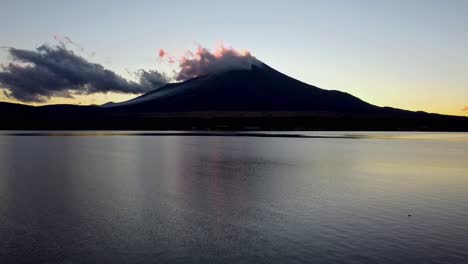 Die-Morgendämmerung-Bricht-über-Einem-Ruhigen-See-An,-Die-Silhouette-Des-Fuji-Steht-Vor-Einem-Leuchtenden-Himmel