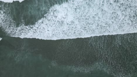 Foamy-ocean-waves-rolling-towards-coastline,-top-down-view