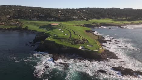 Famous-Pebble-beach-golf-course-over-7th-hole,-cinematic-aerial-view-over-ocean-at-sunrise