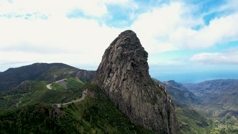 Vista-De-Drones-Del-Roque-De-Agando-Rodeado-De-Exuberante-Vegetación,-Carretera-Con-Curvas,-La-Gomera,-Islas-Canarias,-España
