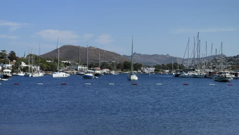 View-of-sailboats-anchored-at-coast-of-Gumusluk-in-sunny-day,-Türkiye