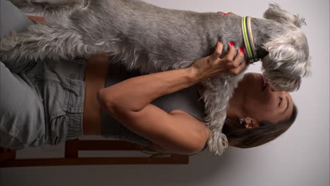 Vertical-slow-motion-of-brunette-hispanic-female-model-petting-her-schnauzer-dog-on-her-lap-and-hugging-it
