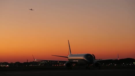 Flugzeug-Auf-Der-Landebahn-In-Der-Abenddämmerung-Mit-Einer-Anderen-Jet-Silhouette-Am-Himmel
