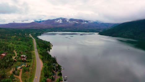 Aerial-Drone-View-of-Beautiful-Mountain-Lake-with-Rolling-Coulds-in-the-Background-as-Cars-Drive-on-Colorado-Highway-Road-Along-the-Shoreline-of-Shadow-Mountain-and-Grand-Lake